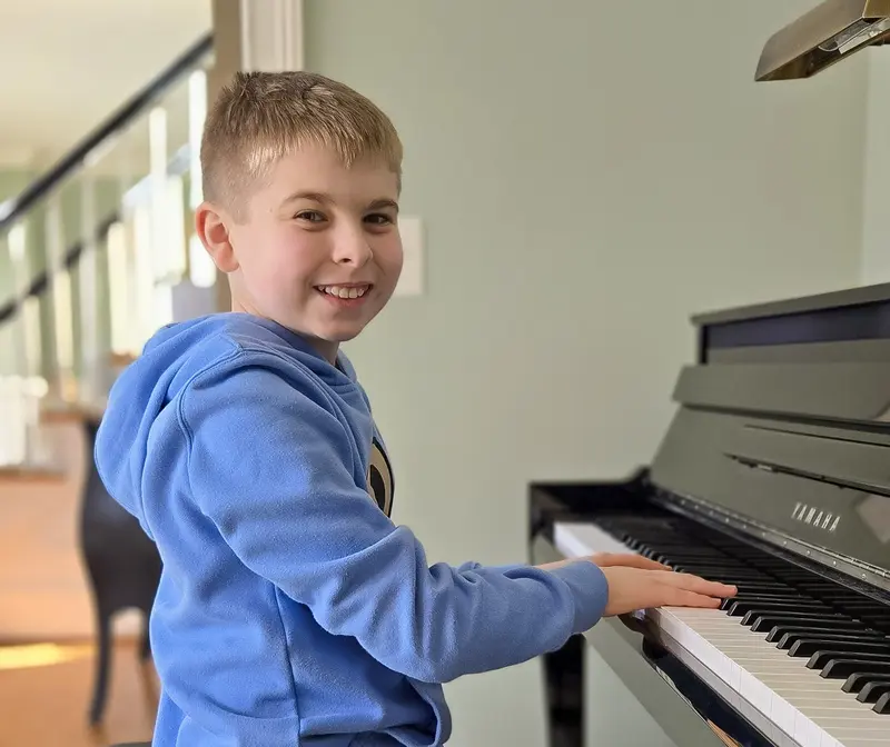 Young piano student smiling at the keys during an in-home lesson